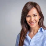 Smiling woman with long brown hair wearing a blue and white striped button-down shirt.