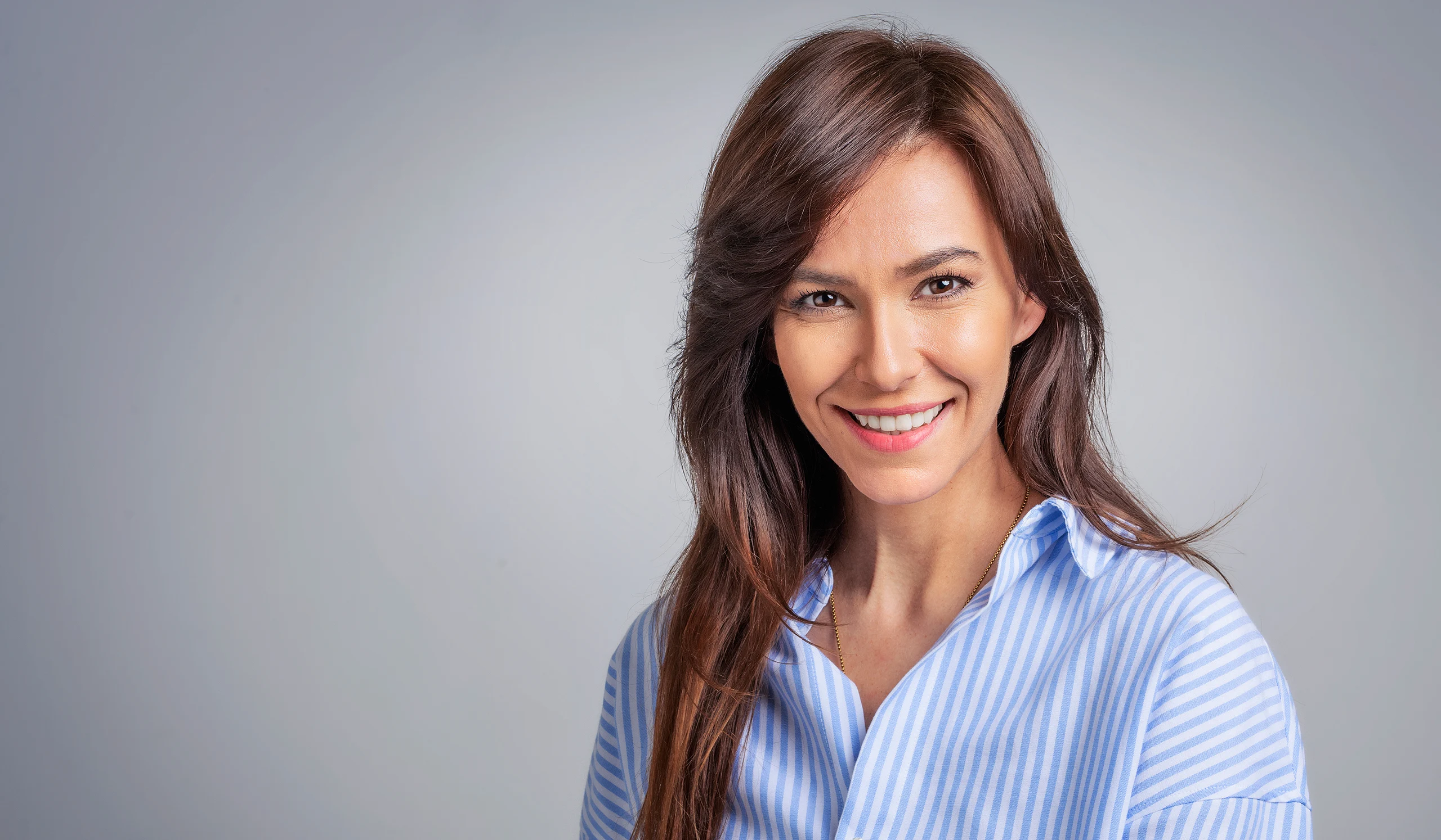 Smiling woman with long brown hair wearing a blue and white striped button-down shirt.