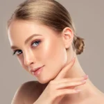 Portrait of a woman with glowing skin and a neat hair bun touching her jawline.
