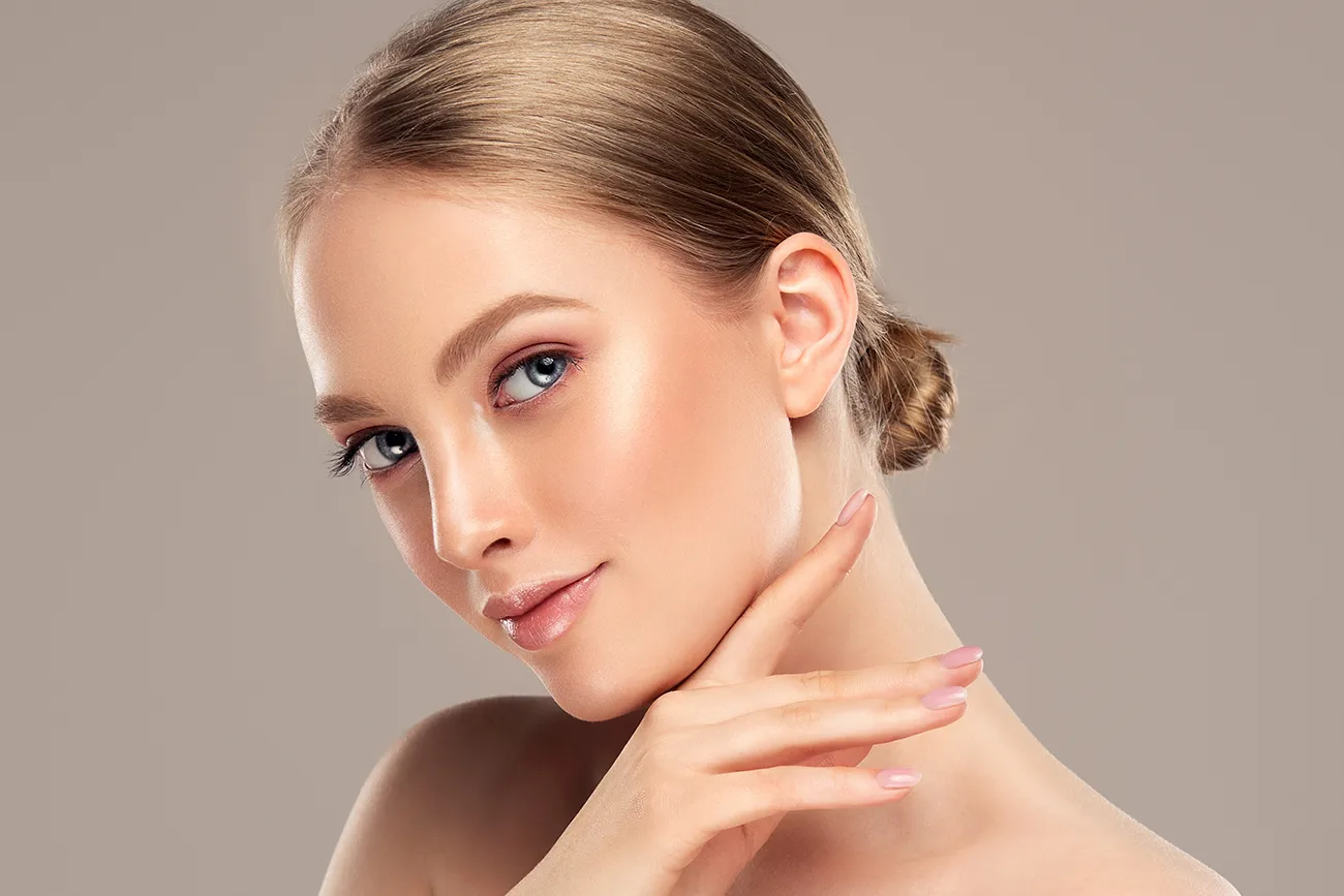 Portrait of a woman with glowing skin and a neat hair bun touching her jawline.
